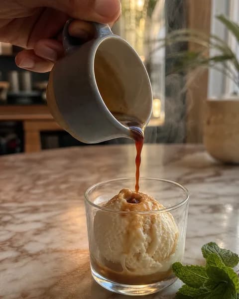 An espresso shot pouring from a small ceramic cup onto a scoop of cream gelato, caught mid-stream.